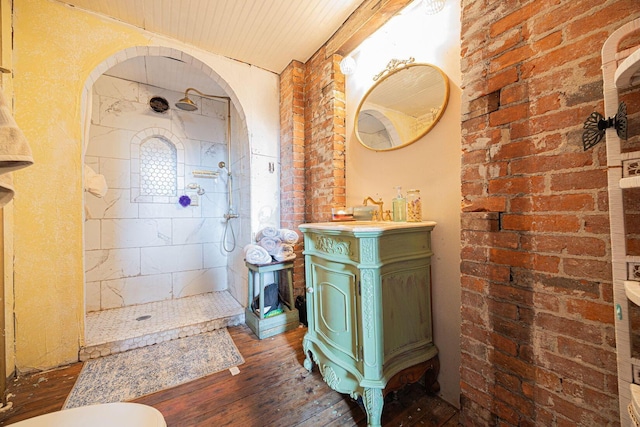 bathroom featuring brick wall, a tile shower, vanity, and hardwood / wood-style floors