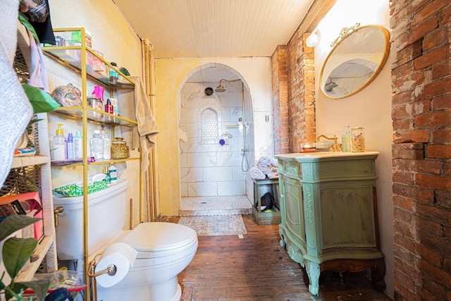 full bathroom with hardwood / wood-style flooring, toilet, vanity, brick wall, and walk in shower