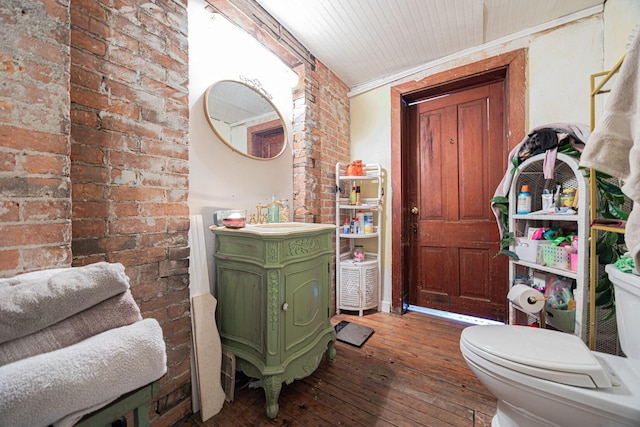 bathroom featuring toilet, brick wall, hardwood / wood-style floors, and vanity