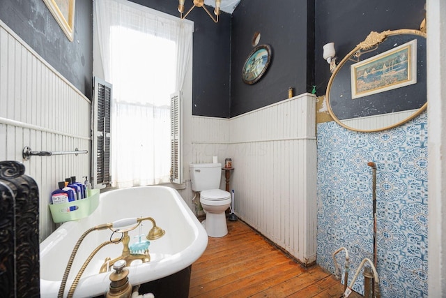 full bathroom with a wainscoted wall, a tub to relax in, hardwood / wood-style flooring, and toilet