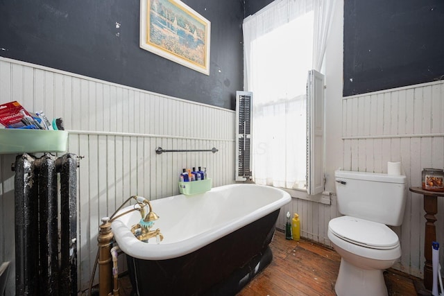 full bathroom with toilet, a wainscoted wall, wood-type flooring, and a freestanding bath