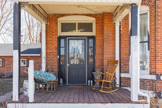 view of exterior entry with brick siding and a porch