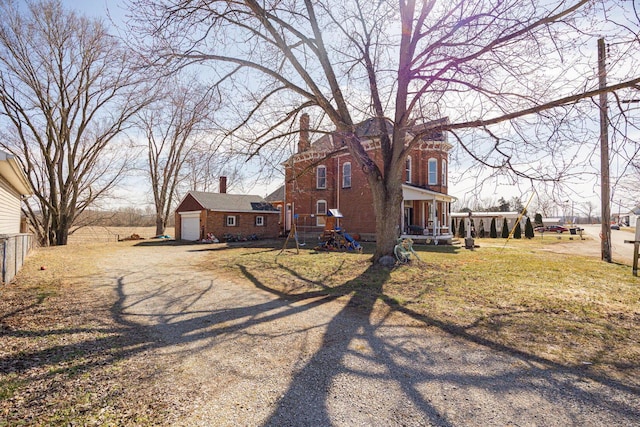 exterior space with driveway, a chimney, an outbuilding, fence, and brick siding