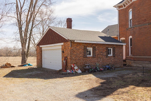 view of property exterior featuring brick siding, a chimney, dirt driveway, a shingled roof, and a garage