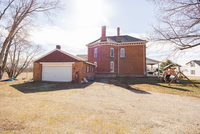 back of property featuring driveway, a garage, a chimney, a playground, and brick siding