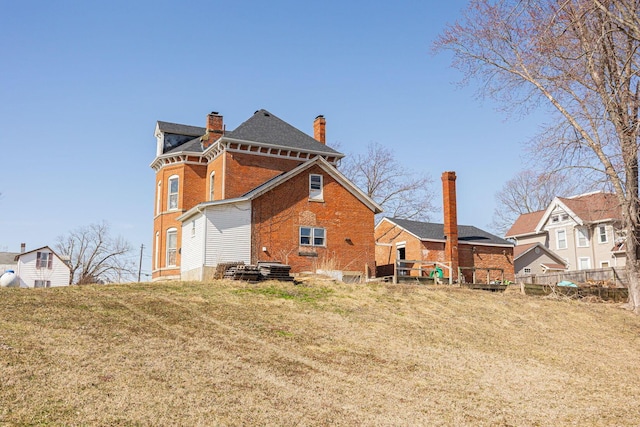 rear view of house with a yard, brick siding, a chimney, and fence