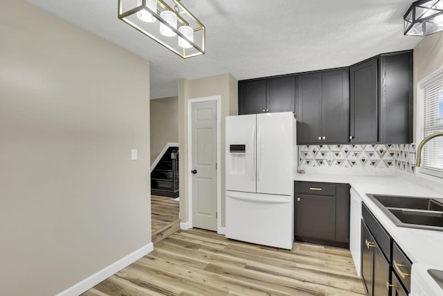 kitchen with white refrigerator with ice dispenser, sink, hanging light fixtures, and light wood-type flooring