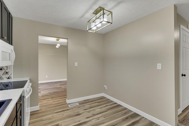 kitchen with white appliances, light hardwood / wood-style floors, hanging light fixtures, and a textured ceiling