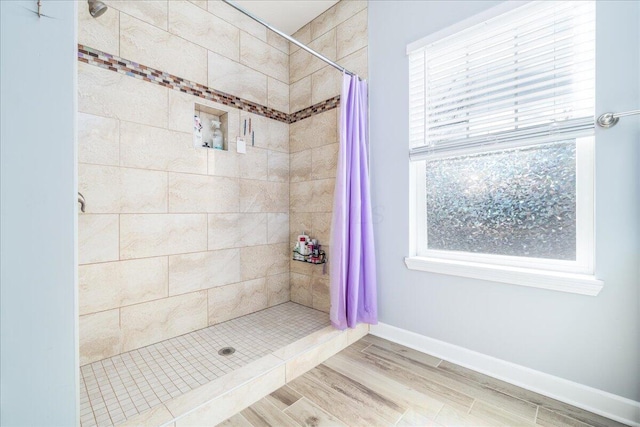 full bathroom with baseboards, a tile shower, and wood finish floors