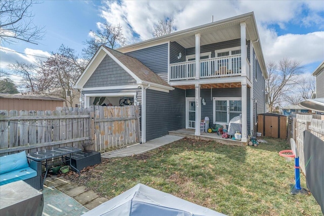 rear view of property with an outbuilding, a balcony, fence, a yard, and a storage unit