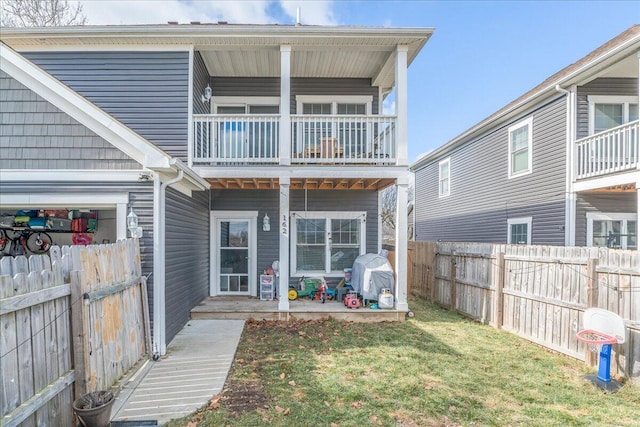 rear view of property with a balcony, a fenced backyard, and a yard