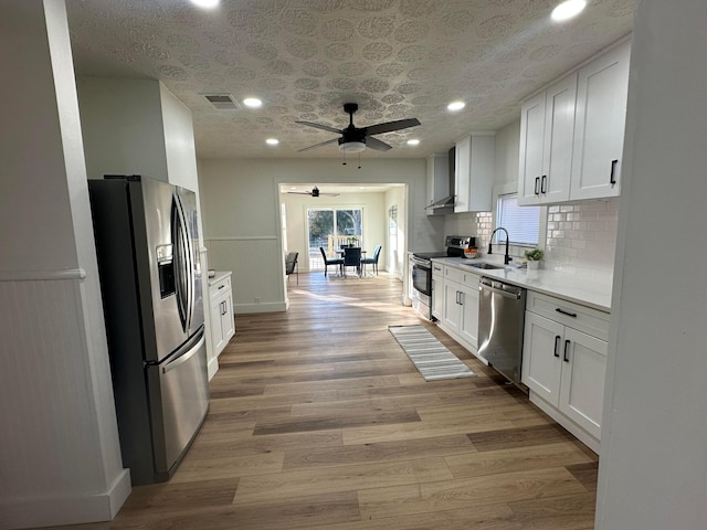 kitchen featuring sink, light hardwood / wood-style flooring, appliances with stainless steel finishes, white cabinets, and wall chimney range hood