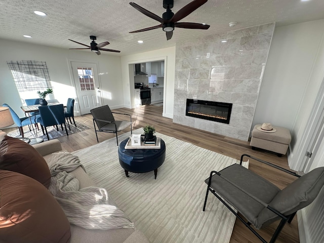 living room featuring a tiled fireplace, sink, light hardwood / wood-style flooring, and a textured ceiling