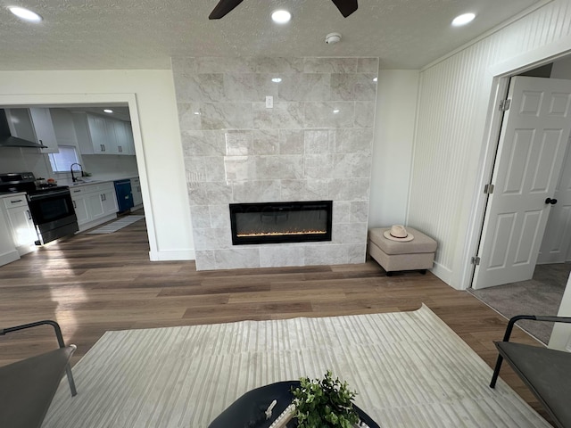 living room featuring wood-type flooring, a tiled fireplace, sink, and a textured ceiling