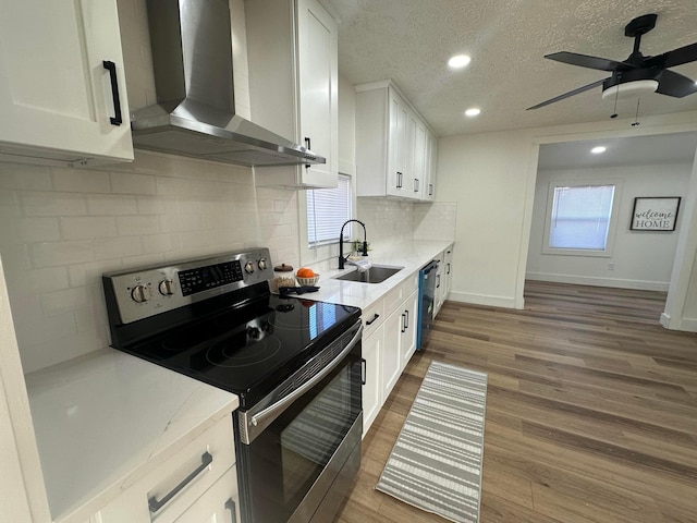 kitchen featuring wall chimney range hood, sink, hardwood / wood-style floors, white cabinets, and stainless steel electric stove