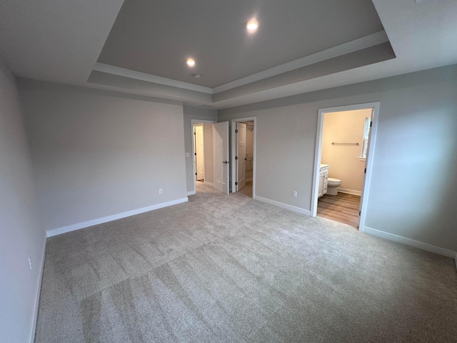 unfurnished bedroom featuring a walk in closet, ensuite bathroom, a raised ceiling, and light carpet