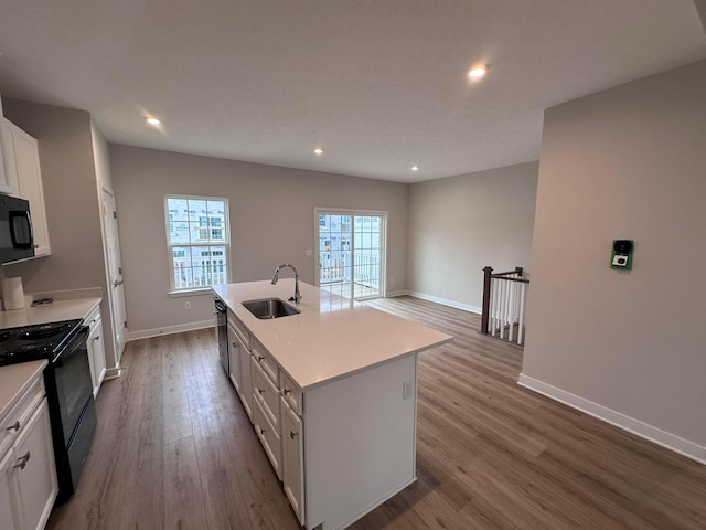 kitchen featuring sink, white cabinetry, light wood-type flooring, an island with sink, and black appliances