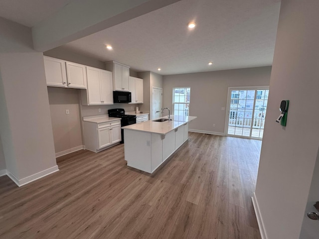 kitchen with sink, white cabinets, a kitchen island with sink, light hardwood / wood-style floors, and black appliances