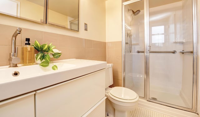 bathroom with a shower with shower door, tile walls, vanity, toilet, and tile patterned floors