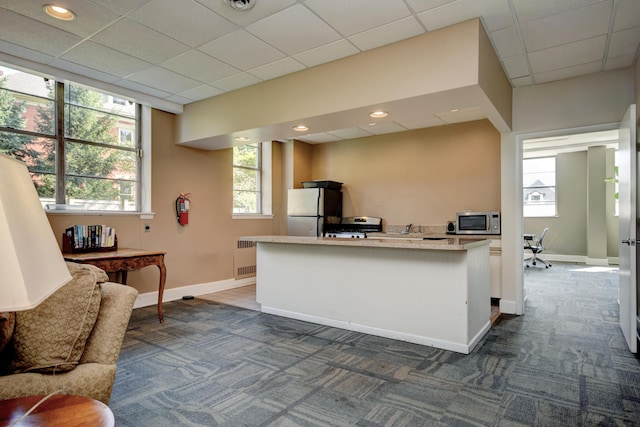 interior space with appliances with stainless steel finishes, radiator, a drop ceiling, and dark carpet