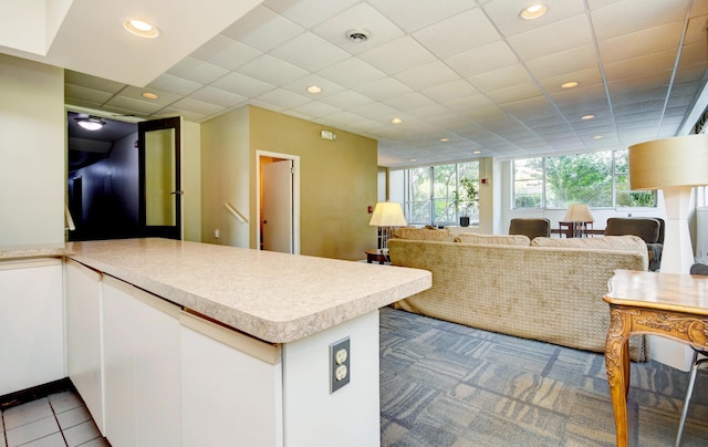 kitchen featuring a paneled ceiling, kitchen peninsula, light tile patterned floors, and white cabinets