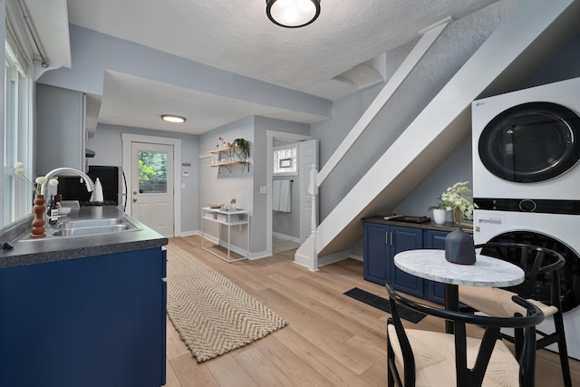 kitchen featuring blue cabinetry, stacked washer and clothes dryer, light hardwood / wood-style floors, and sink