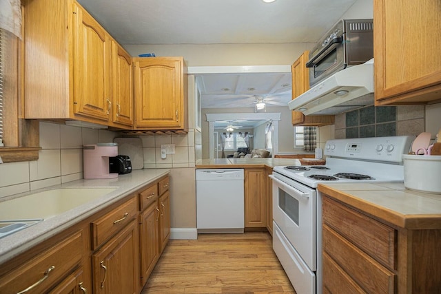 kitchen with white appliances, kitchen peninsula, decorative backsplash, and light wood-type flooring