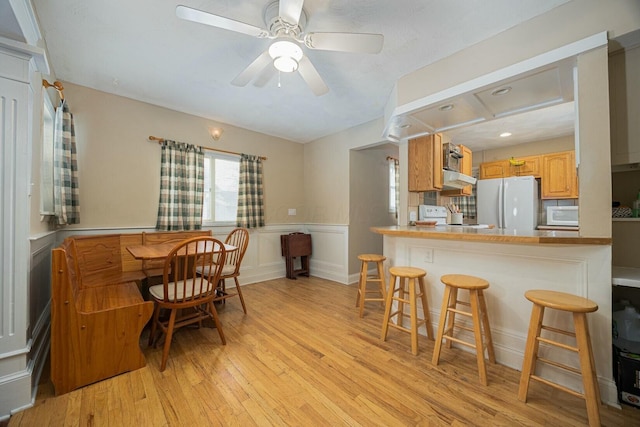 kitchen featuring white appliances, ceiling fan, a kitchen breakfast bar, kitchen peninsula, and light wood-type flooring