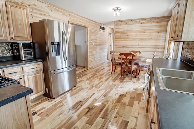 kitchen featuring sink, light hardwood / wood-style flooring, stainless steel fridge, wooden walls, and light brown cabinets