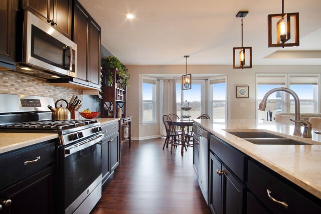 kitchen with sink, appliances with stainless steel finishes, dark hardwood / wood-style flooring, pendant lighting, and decorative backsplash