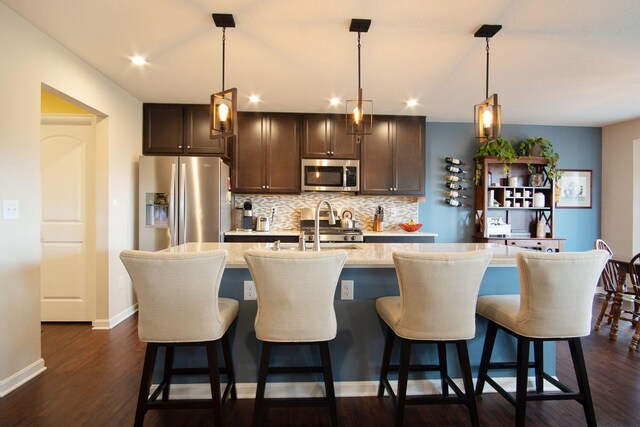 kitchen with tasteful backsplash, hanging light fixtures, stainless steel appliances, dark wood-type flooring, and a center island with sink