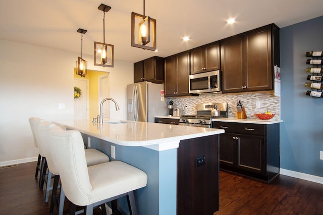 kitchen with sink, hanging light fixtures, backsplash, stainless steel appliances, and a center island with sink