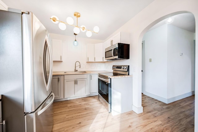 kitchen with sink, light wood-type flooring, appliances with stainless steel finishes, pendant lighting, and white cabinets