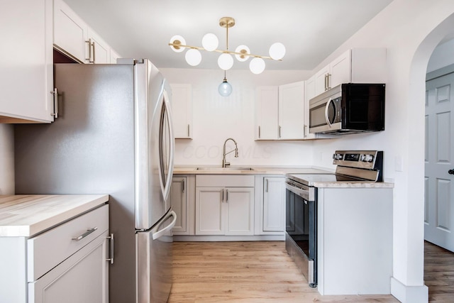 kitchen featuring sink, decorative light fixtures, stainless steel appliances, light hardwood / wood-style floors, and white cabinets