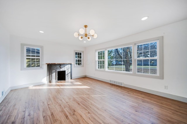 unfurnished living room featuring a premium fireplace, a chandelier, and light wood-type flooring