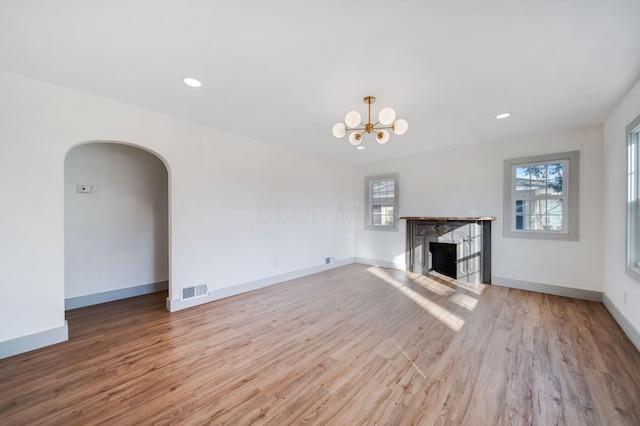 unfurnished living room featuring an inviting chandelier, a wealth of natural light, and light wood-type flooring