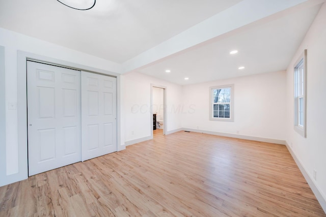 unfurnished bedroom featuring beamed ceiling, a closet, and light wood-type flooring