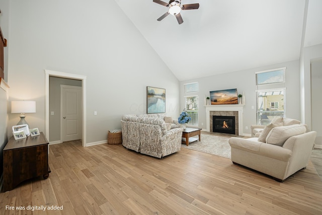 living room featuring a tile fireplace, ceiling fan, high vaulted ceiling, and light hardwood / wood-style flooring