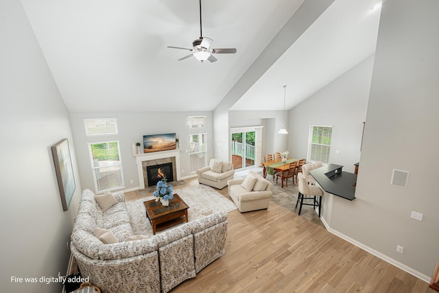 living room featuring a tiled fireplace, high vaulted ceiling, ceiling fan, and light wood-type flooring