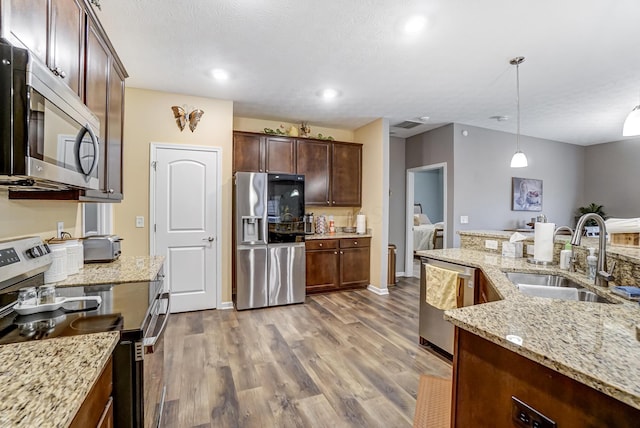 kitchen featuring sink, light stone counters, hanging light fixtures, stainless steel appliances, and hardwood / wood-style floors