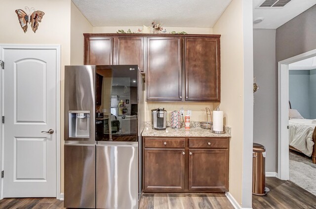 kitchen featuring dark wood-type flooring, light stone counters, stainless steel fridge with ice dispenser, and a textured ceiling