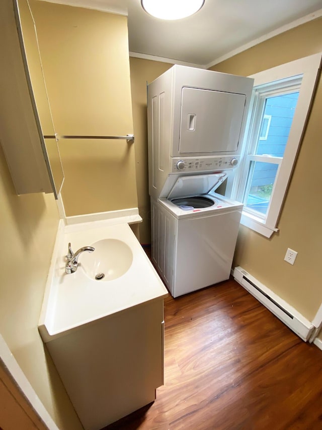 laundry area with sink, stacked washer / dryer, wood-type flooring, ornamental molding, and a baseboard radiator