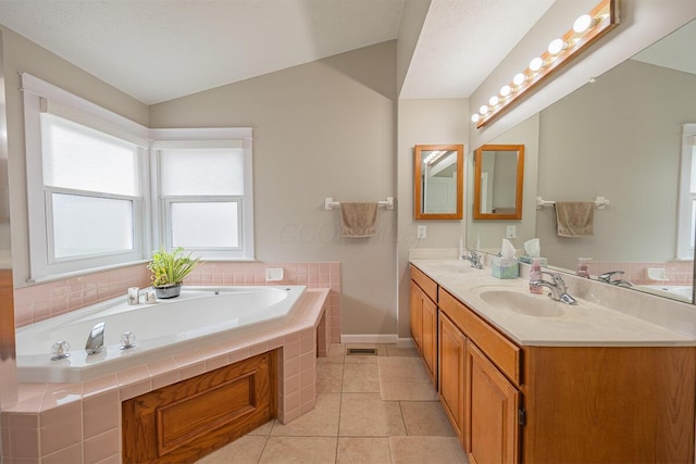 bathroom with tile patterned flooring, vanity, a relaxing tiled tub, and vaulted ceiling