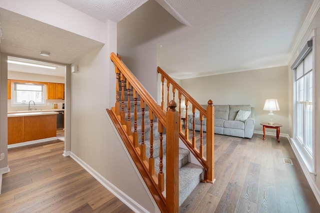 stairs featuring sink, wood-type flooring, and a textured ceiling