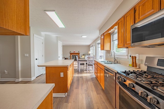 kitchen with a kitchen island, sink, light wood-type flooring, stainless steel appliances, and a textured ceiling