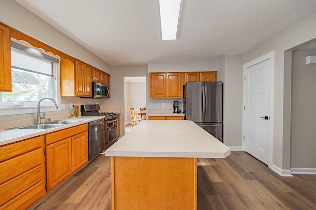 kitchen with sink, hardwood / wood-style flooring, stainless steel appliances, a center island, and a textured ceiling