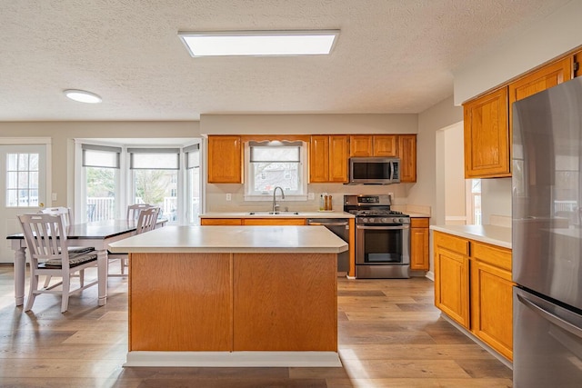 kitchen featuring appliances with stainless steel finishes, a center island, sink, and light wood-type flooring