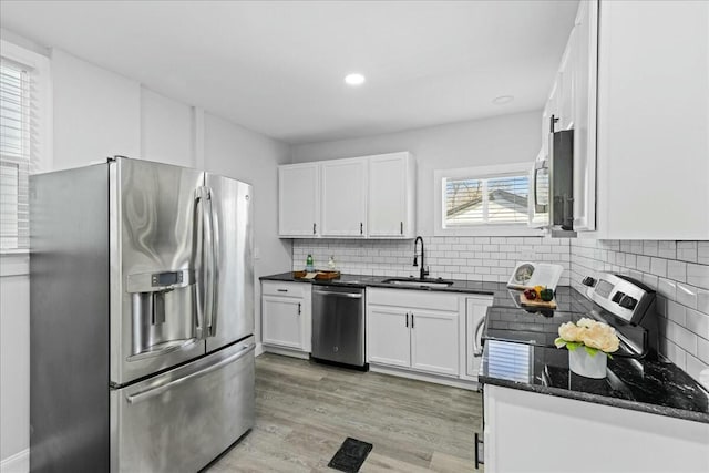 kitchen with appliances with stainless steel finishes, white cabinetry, sink, decorative backsplash, and light wood-type flooring