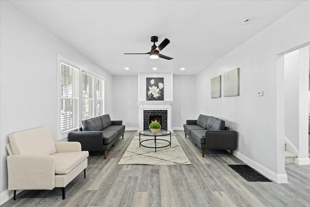 living room featuring ceiling fan, a fireplace, and light hardwood / wood-style flooring