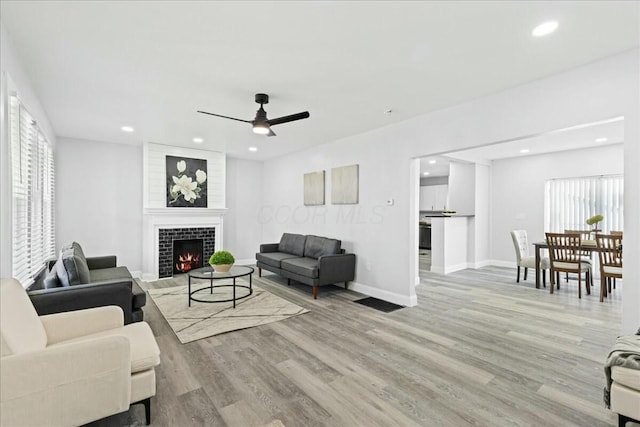 living room featuring ceiling fan, a large fireplace, and light wood-type flooring